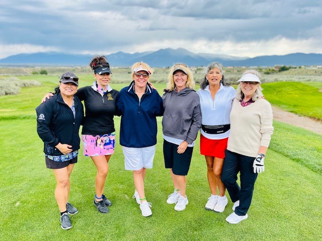 Six women golfers smiling on a golf course in Albuquerque with Sandia Mountains in the background