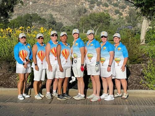 Women golfers from Albuquerque in hot air balloon-themed uniforms posing at the California Match with hills and flowers in the background