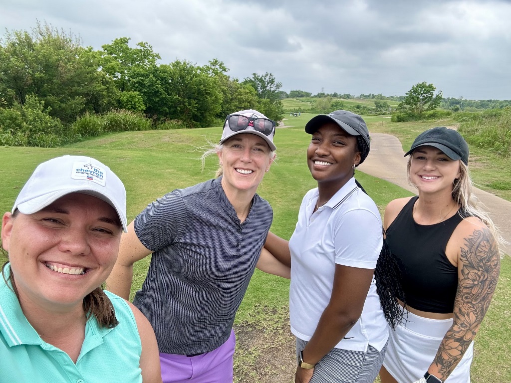 Four female golfers posing for a selfie on a tee box in Houston Texas