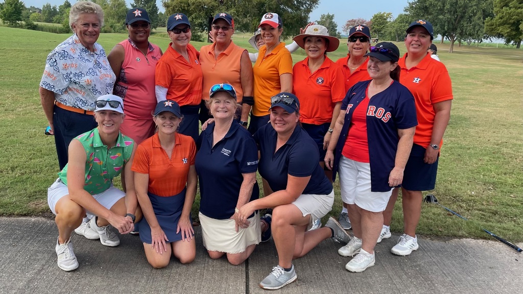 A team of female golfers taking a group photo before a golf competition in Houston Texas. They are wearing Houston Astros colors!